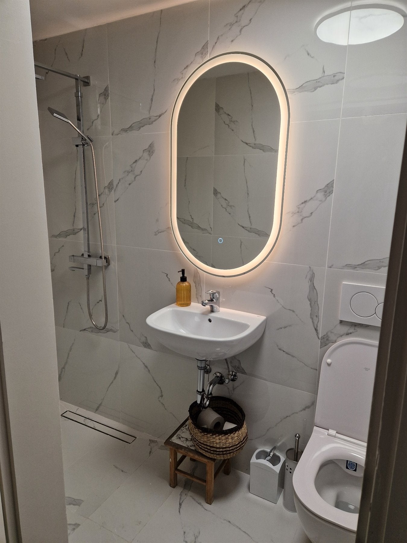Oval LED mirror above the washbasin in a bright marble bathroom.