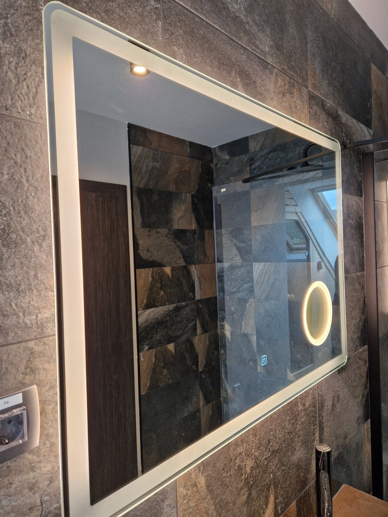 Large rectangular LED mirror in a bathroom with stone tiles.