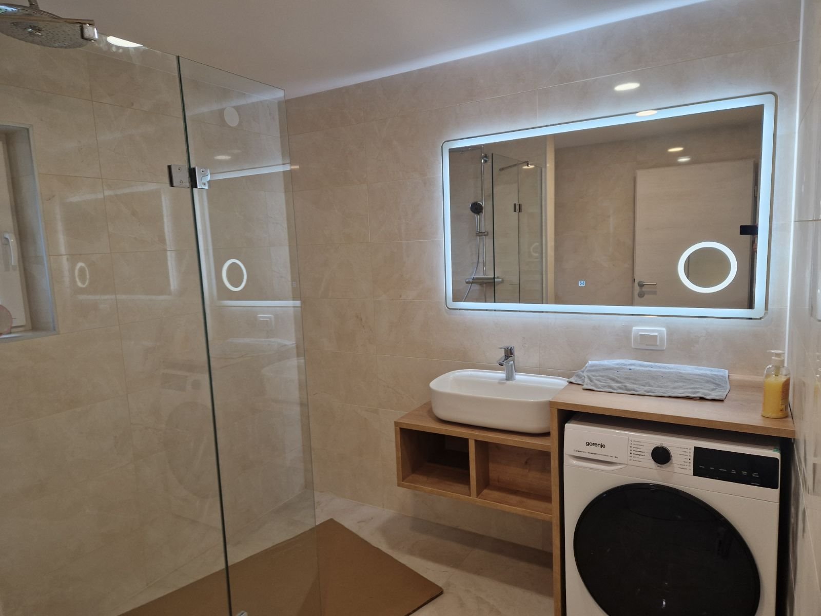 Rectangular LED mirror above the washbasin in a bathroom with a shower wall.