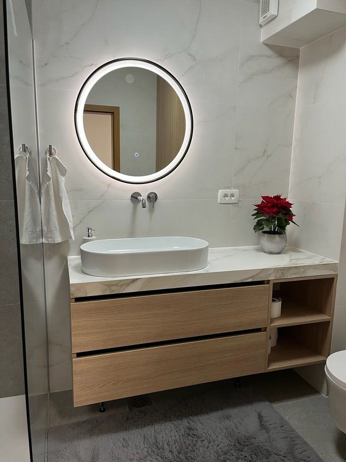 Round LED mirror with a black frame above the washbasin in a bright bathroom.